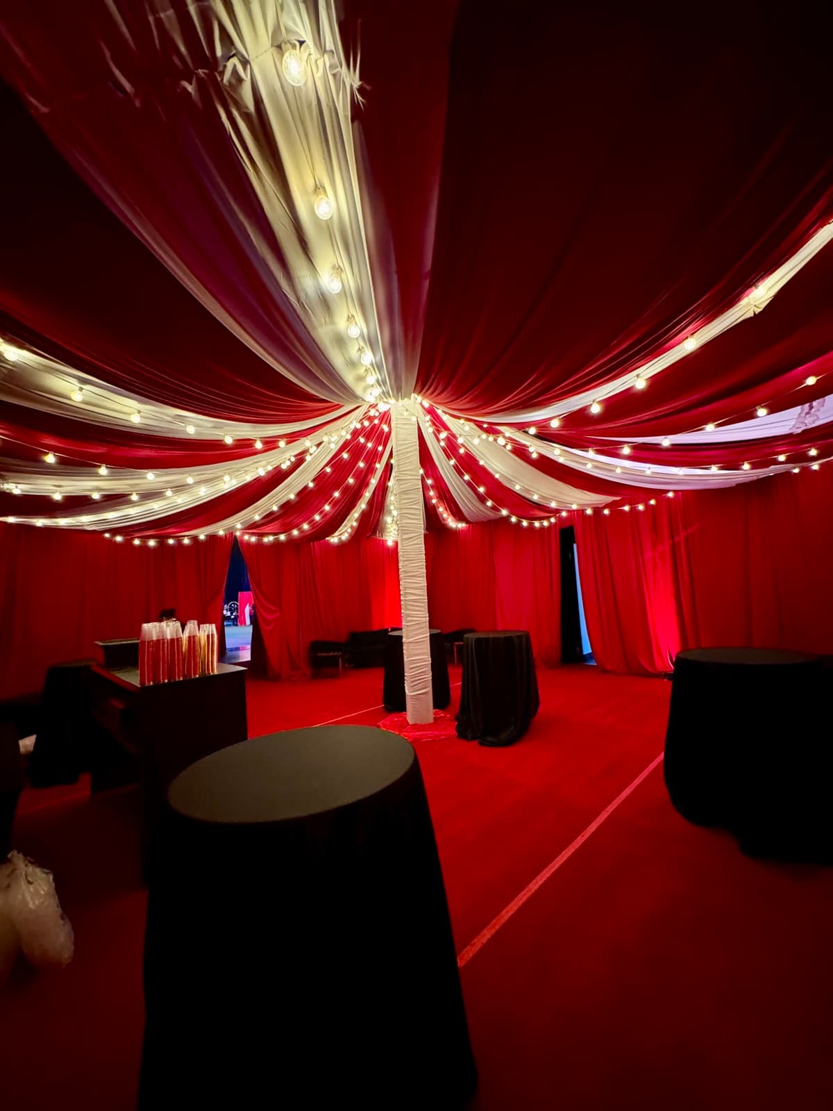 Red and white circus-style tent draping with string lights over a lounge area