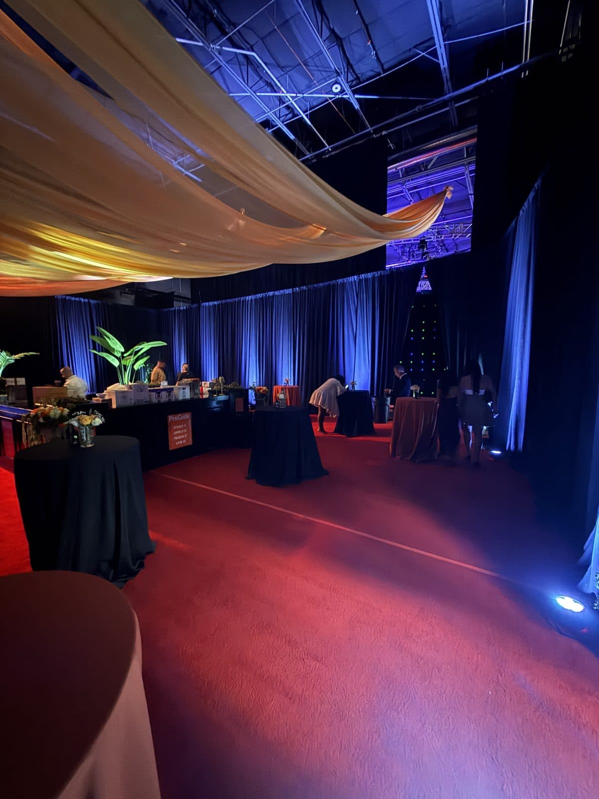 Corporate gala with ceiling drape swag and blue uplighting over a red carpet event floor